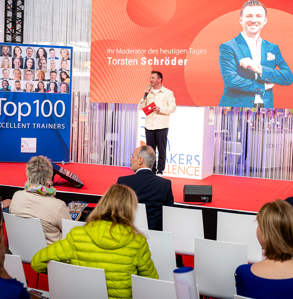 Torsten Schröder steht auf der Bühne, im Hintergrund ist ein Bild zu sehen, welches ihn als Moderation des Tages vorstellt