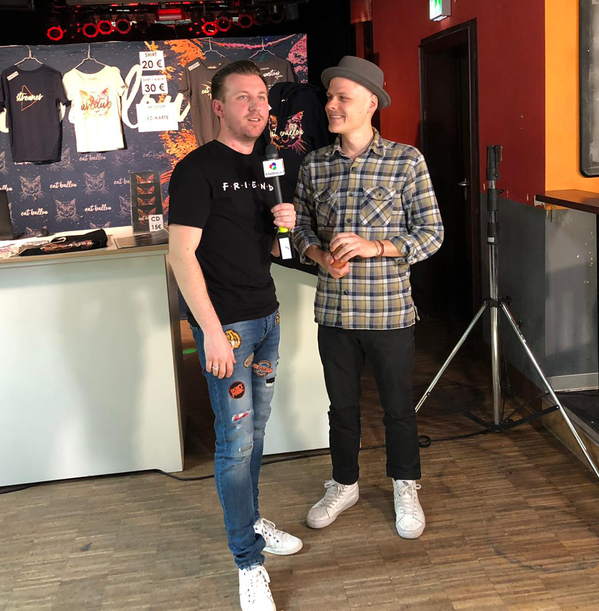 Torsten Schröder steht vor einem Merch-Stand und interviewt einen Mann